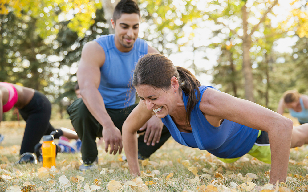 People in a field working out with a man encouraging a woman to do push ups