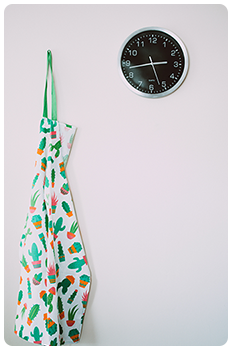 Clock on kitchen wall with an apron hanging next to it