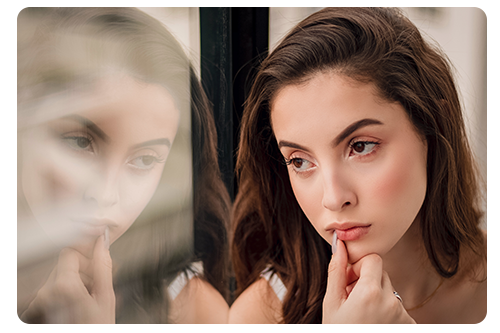 Woman next to window with hand on face lost in thought