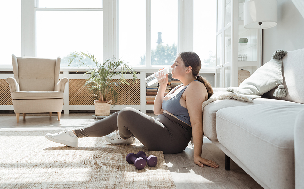 A woman working out in her living room taking a break and drinking water